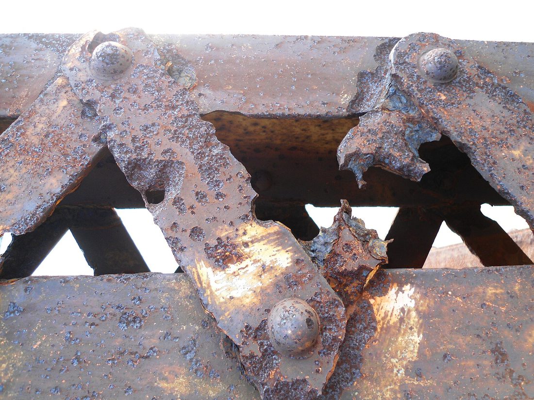 Heavily rusted iron girders, the orange-brown flaking surface covering what was once smooth grey metal.